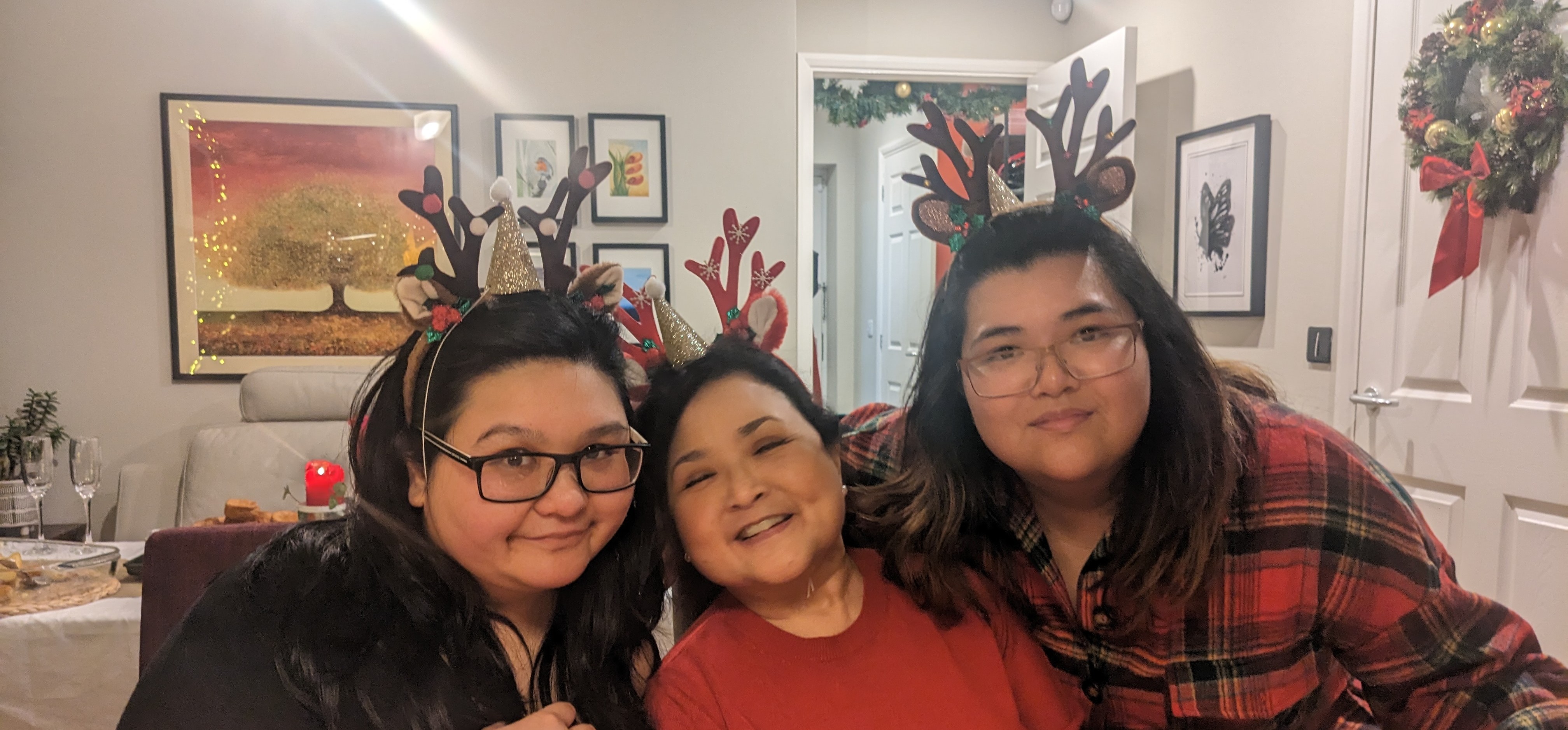 Anna with her mum and sister, smiling with reindeer headbands at Christmas